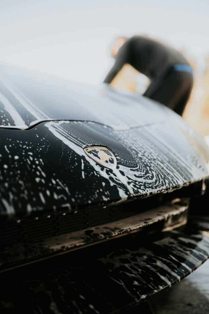 Close-up of a luxury sports car under soap suds during a detailed wash.